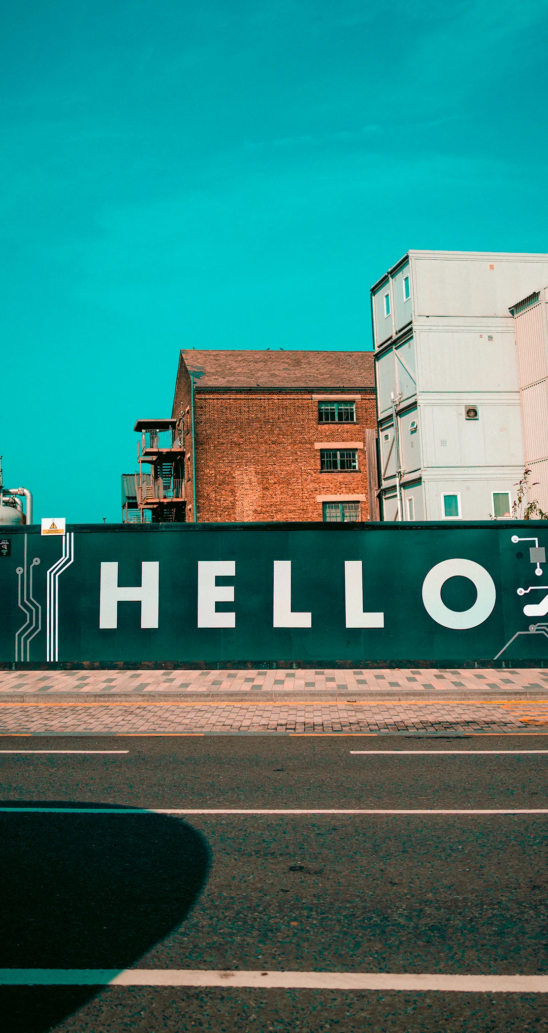 A HELLO hoarding beneath a warehouse and a white block under blue sky