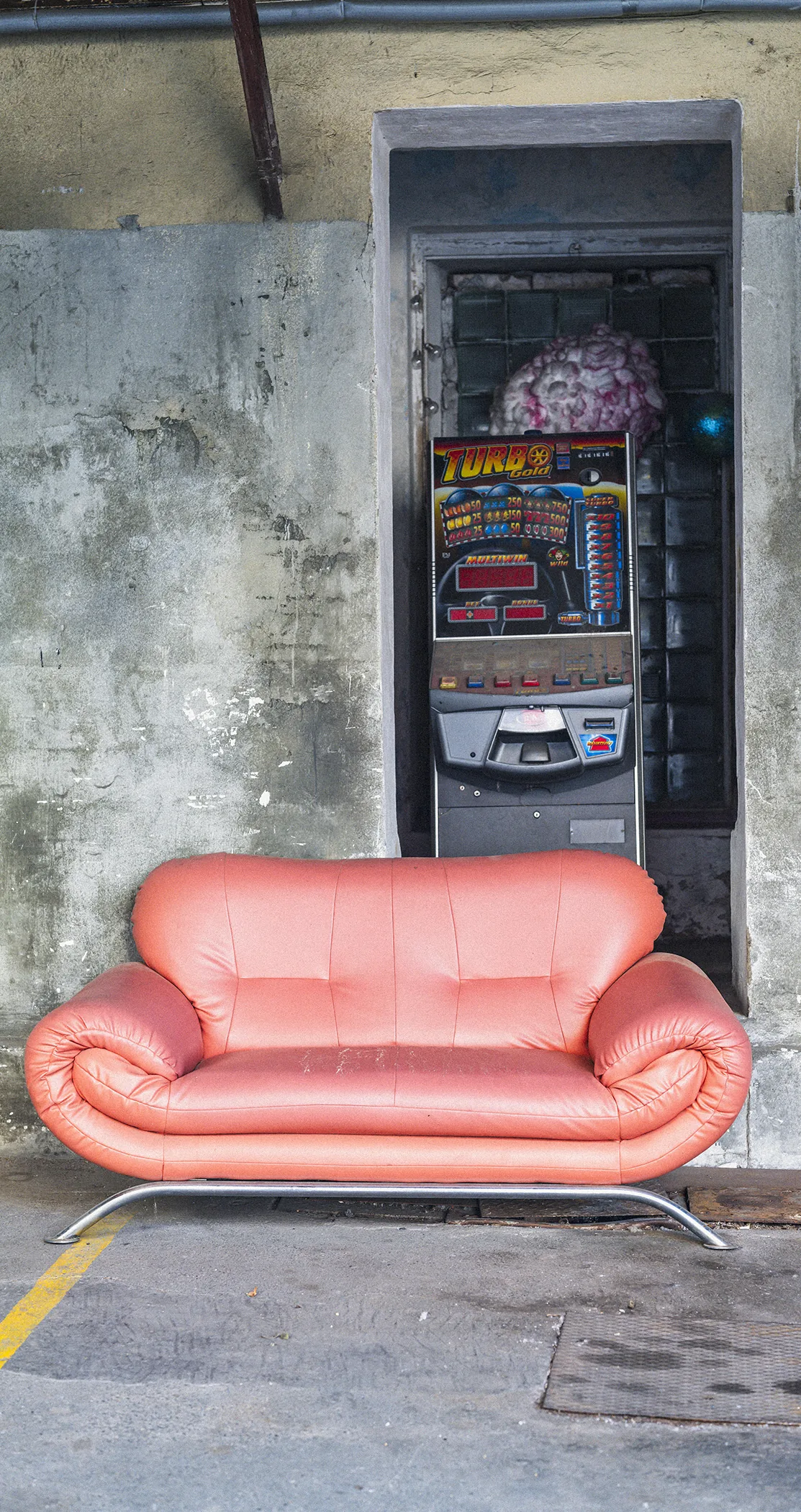 A pink leather sofa left beside a fruit machine in a concrete doorway