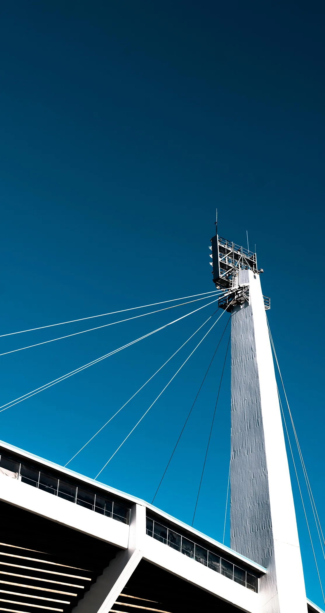 A stadium floodlight mast and its cables rising into a blue sky, Gothenburg