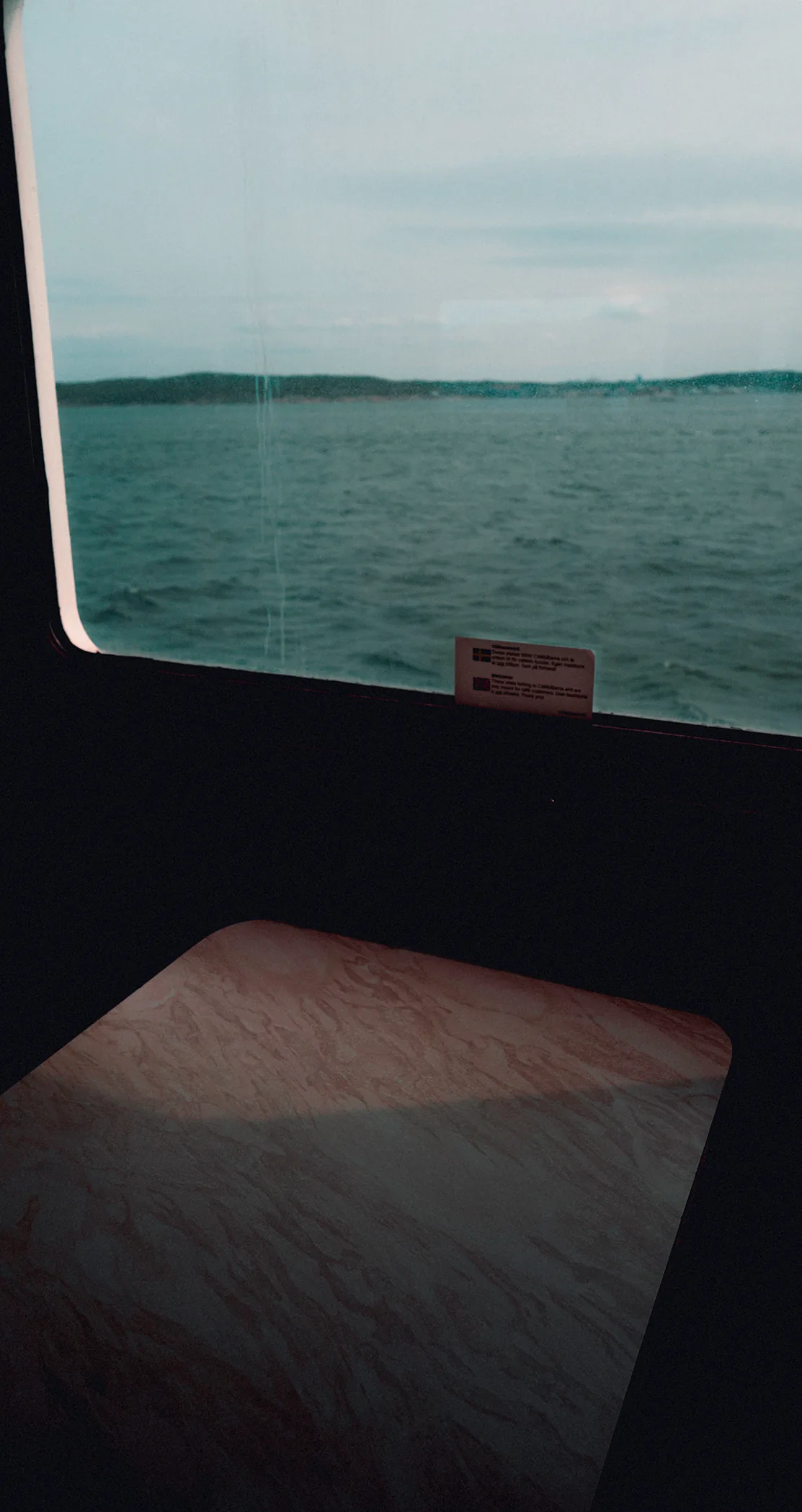 Grey sea and a low shoreline through a ferry window above a dark table