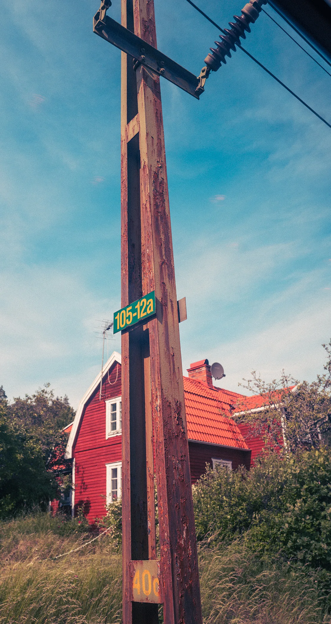 A weathered wooden pole with a green marker sign in front of a red wooden house